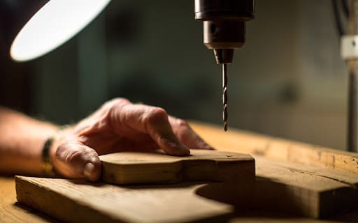 woodworking project under a drill being guided by an elderly man