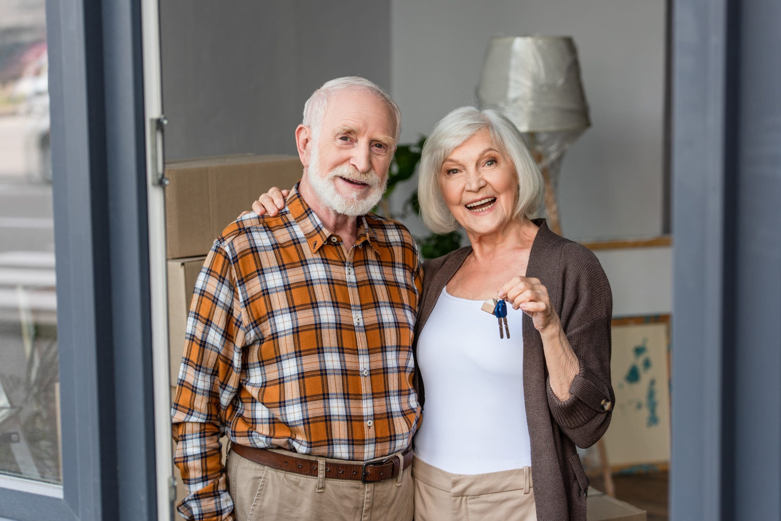laughing senior woman holding keys and embracing husband in new house